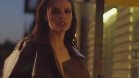 Stylish model in brown jacket turns to camera over night city background Stock Footage 159984707