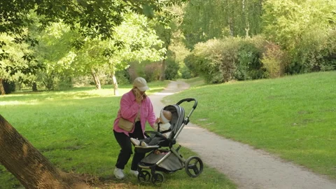Stylish mother talks on the phone while walking in the park with her young child Stock Footage 234319018