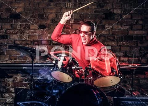 Stylish musician in sunglasses emotionally playing drums against brick wall Stock Photos
