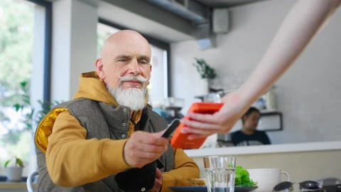 A stylish old man makes a purchase in a coffee shop, pays with a bank card Stock Footage 246901127