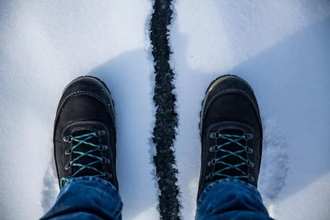 A stylish pair of black boots featuring blue laces is standing in the snow Stock Photos