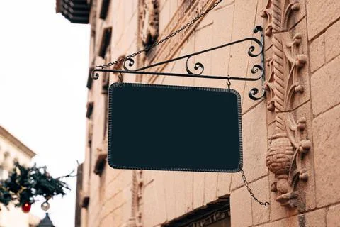Stylish rectangular blank sign in a wrought-iron frame hangs on the stone wall 写真素材