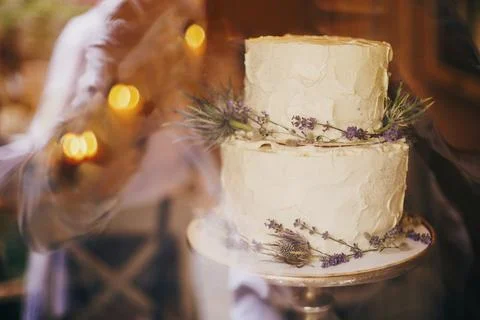 Stylish rustic wedding cake with lavender and thistle decor on table at wed.. Stock Photos