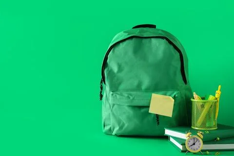 Stylish school backpack with different stationery and alarm clock on green ba Stock Photos