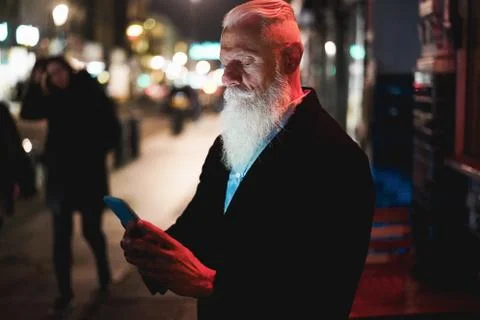 Stylish senior man using smartphone standing in city street with bokeh lights Stock Photos