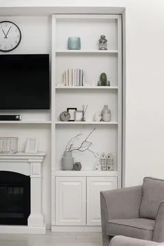 Stylish shelves with different decor elements, fireplace and TV set in room.. Stock Photos