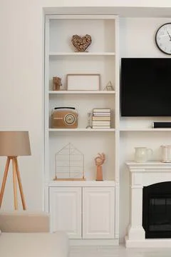 Stylish shelves with different decor elements and TV set in room. Interior .. Stock Photos
