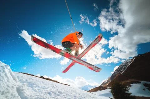 Stylish skier in orange jacket does a leap of crossing skis in flight against Stock Photos