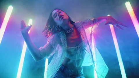 Stylish slim woman dancing backlit colorful neon light lamps, haze and glow Stock Footage 237690853