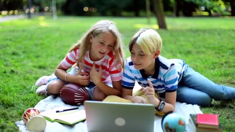 Stylish smiling kids using laptop resting in sunny green park outside. Learning  Video stock 137327045