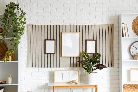 Stylish striped rug with frames hanging on white brick wall in light living r Фото