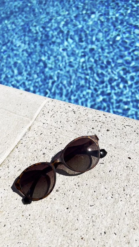 Stylish Sunglasses on Poolside Edge with Blue Water Background Stock Footage 303412335