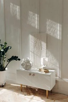 Stylish white bedside table with decor, lamp and white abstract gypsum painting Stock Photos