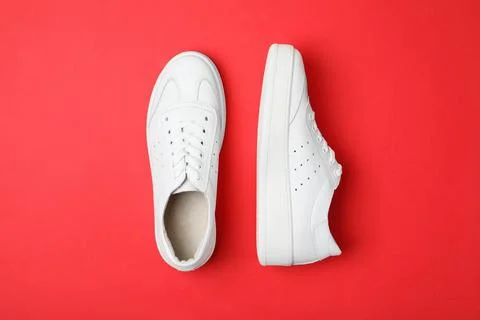 Stylish white shoes on red background, flat lay Stock Photos