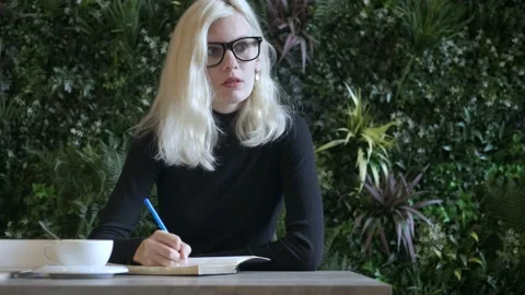 Stylish woman writes in a diary while sitting in an eco cafe 스톡 동영상 163635281