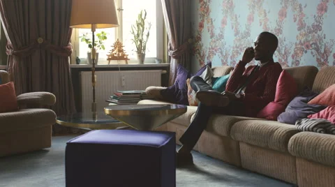 Stylish Young Black Man Sitting on Sofa and Talking on Cellphone Video stock 59864167