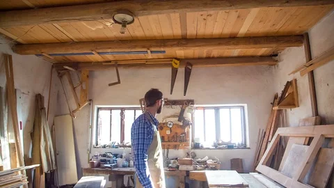 A stylish young carpenter with a beard and glasses smiling at his workplace Stock Footage 89661764