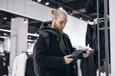 Stylish young man with beard selecting a hat in a modern clothing store. Stock Photos