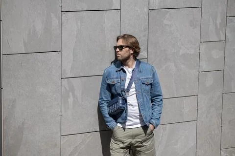 A stylish young man in a denim jacket, white T-shirt, and shorts poses conf.. Фото