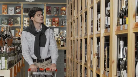 Stylish young man exploring wine selections with a shopping cart Stock Footage 311986403