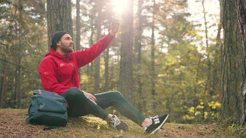 Stylish young man in hat and red jacket sitting in woods sunny day, and makes Stock Footage 147065923