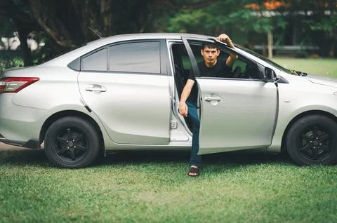Stylish Young Man Posing with Silver Sedan on Green Grass Surface Foto stock