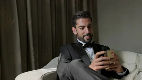 Stylish Young Man Sitting On Sofa With Cellphone In Hands. Man In Suit And White Stock-Footage 153700539