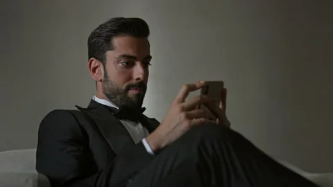Stylish Young Man Sitting On Sofa With Cellphone In Hands. Man In Suit And White Stock Footage 153710370