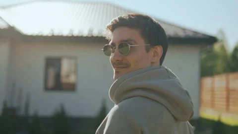 Stylish young man standing in the yard in sunglasses on a sunny day Stock Footage 247472062