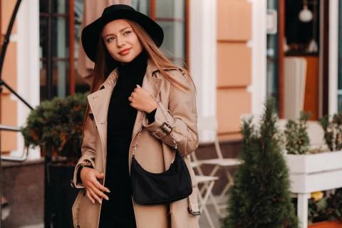 Stylish young woman in a beige coat and black hat and with a black purse on a Stock Photos