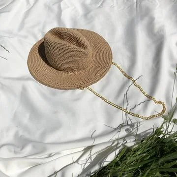 Stylishly Designed Straw Hat Adorned with a Chain on a Soft Fabric Background Stock Photos