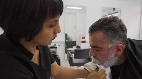 Stylist with african client making faces while drying his beard.MOV Stock Footage 255797365
