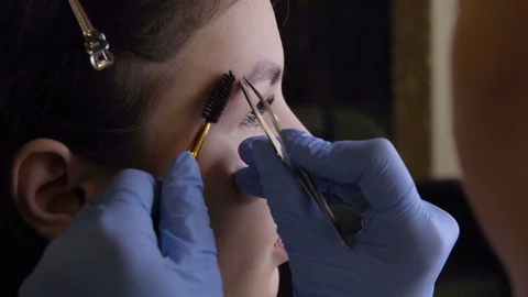 Stylist does beautiful eyebrows to the young beautiful woman. Beauty shop. Close Stock Footage 73944234