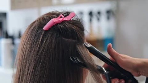 Stylist using flat iron on long brown hair in salon Stock Footage 346658365