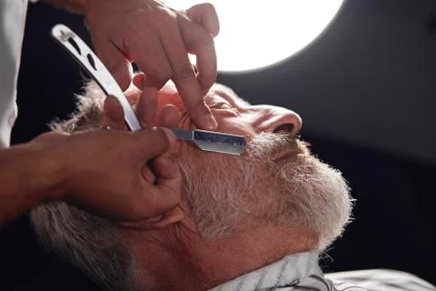 Stylist using a traditional tool to shave facial hair on face Stock Photos