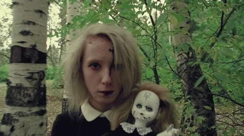 Stylized shot creepy white faced woman with a doll in the grass in the woods Stock Footage 67461399