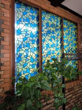 A stylized window with a mosaic geometric pattern against a brick wall 스톡 사진