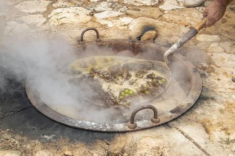 Submerging wire basket of white grapes in boiling cauldron during tradition.. Stock Photos