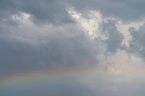 Subtle rainbow arcs beneath storm clouds, dampened light and soft color band  Stock Photos