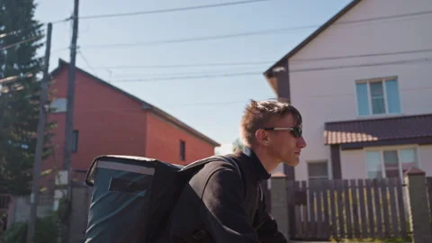 Suburban delivery rider with backpack under sunny blue sky, Bike messenger Stock Footage 331253378