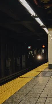 Subway train approaching a station platform with bright headlight in a dark Stock Photos