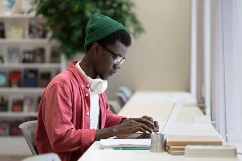 Successful African American guy programmer is typing code in laptop sits in Stock Photos