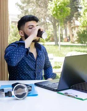 Successful boy with beard sitting at table, working outdoors. Stock Photos