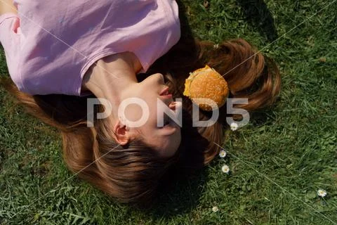 Successful business woman lying on grass with fast food burger cheesburger on Stock Photos