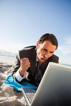 Successful businessman lying on the beach while using his laptop Photos