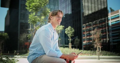 Successful handsome Caucasian guy sitting on bench enjoying coffee using Stock Footage 136674475