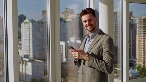 A successful happy man in a nice suit in the office near the window with phone Stock Footage 246748408