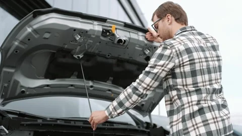 Successful male customer looking inside opened car hood of silver electric car Stock Footage 249670097