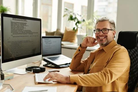 Successful mature IT engineer looking at camera by workplace Stock Photos
