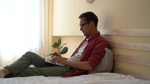 Successful relaxed man programmer typing code lying on bed with laptop on lap Stock Footage 227063330